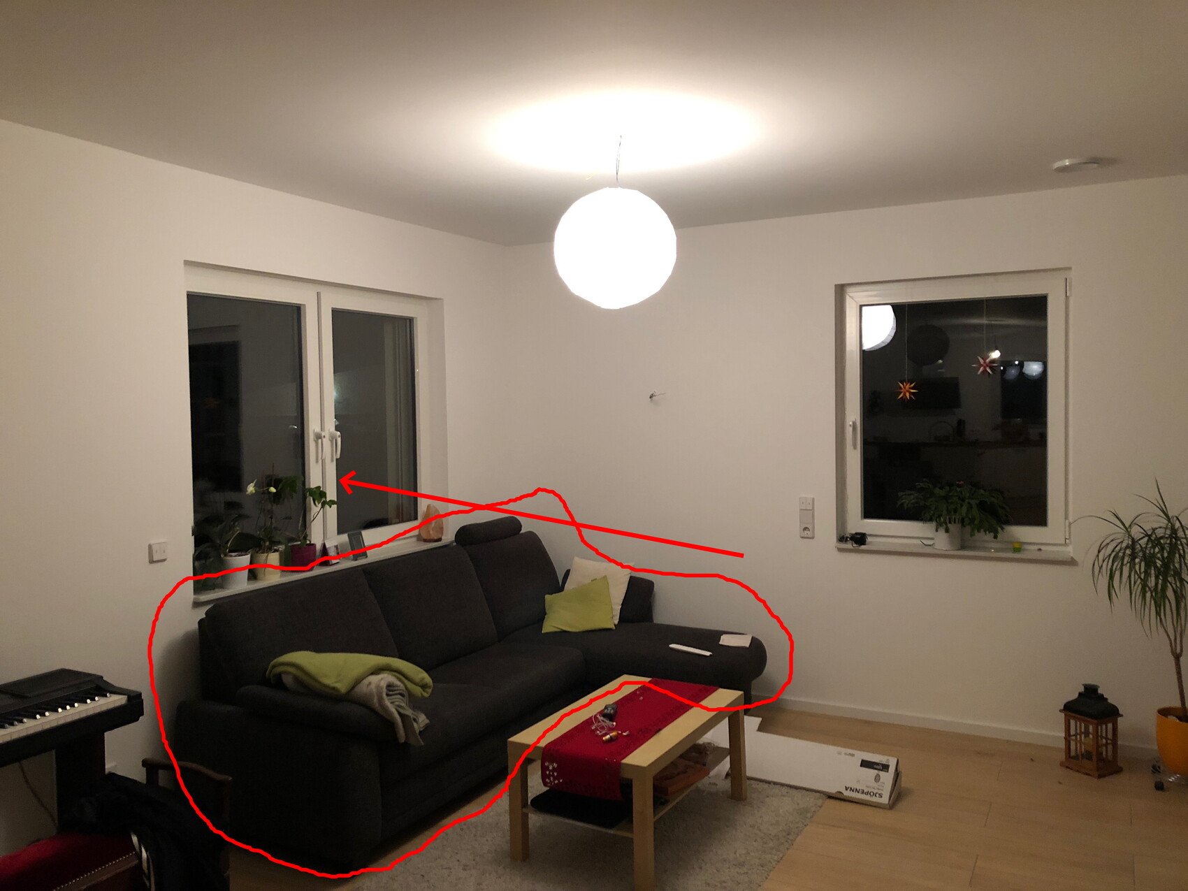 Wohnzimmer mit dunkler Eckcouch, Holztisch mit rotem Läufer, Pflanzen und Pendelleuchte.