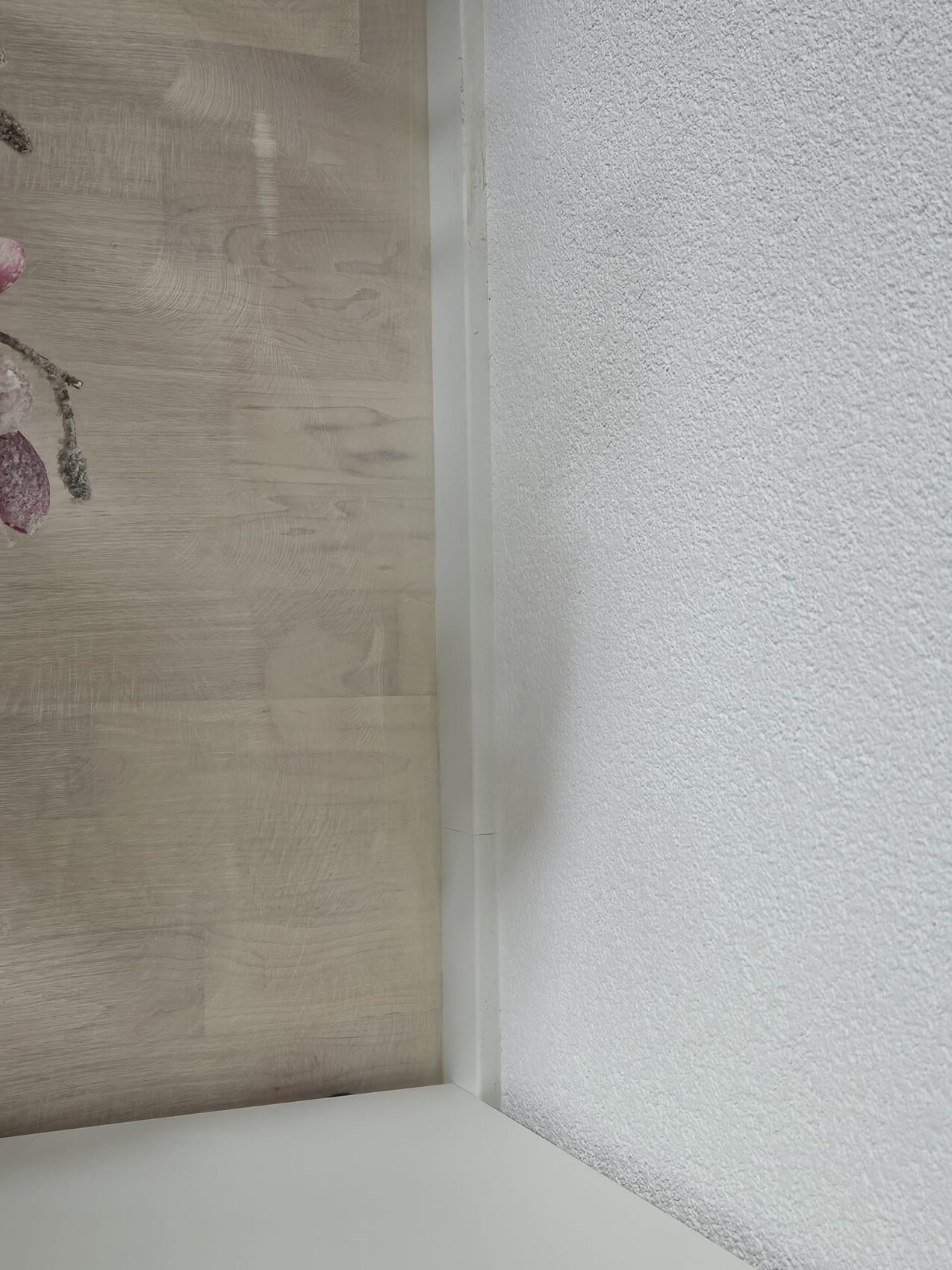 Ecke eines Raums: linke Holzpaneelwand, rechte grob strukturierte weiße Wand, weiße Stoßleiste.