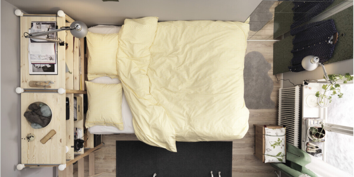 Schlafzimmer mit Bett, gelb gestreifte Bettwäsche, Schreibtisch und Pflanze