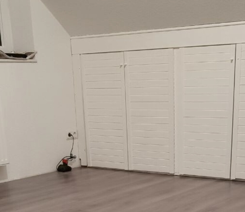 Raum mit weißen Lamellentüren eines Schranks, hellem Laminatboden; Kabel am Boden