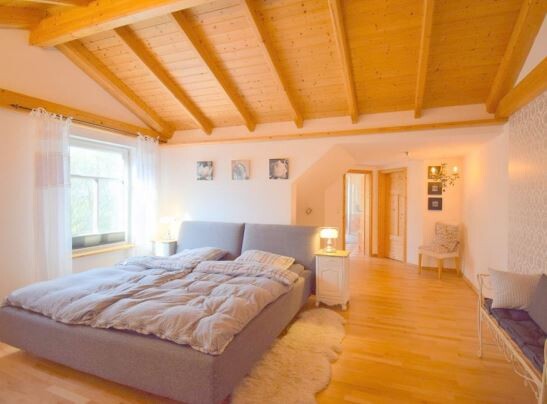 Schlafzimmer mit Holzbalkendecke, großem Bett, Nachttischen, Lampen und Fenster.