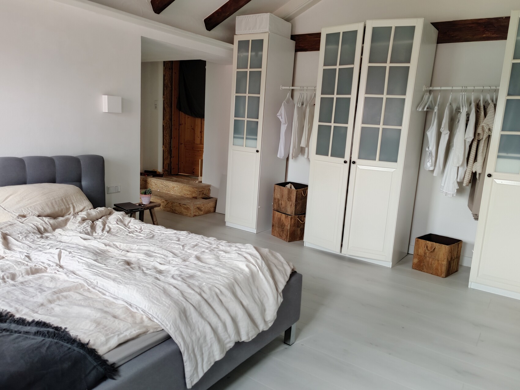 Helles Schlafzimmer mit grauem gepolstertem Bett, beiger Decke, weißen Kleiderschränken.