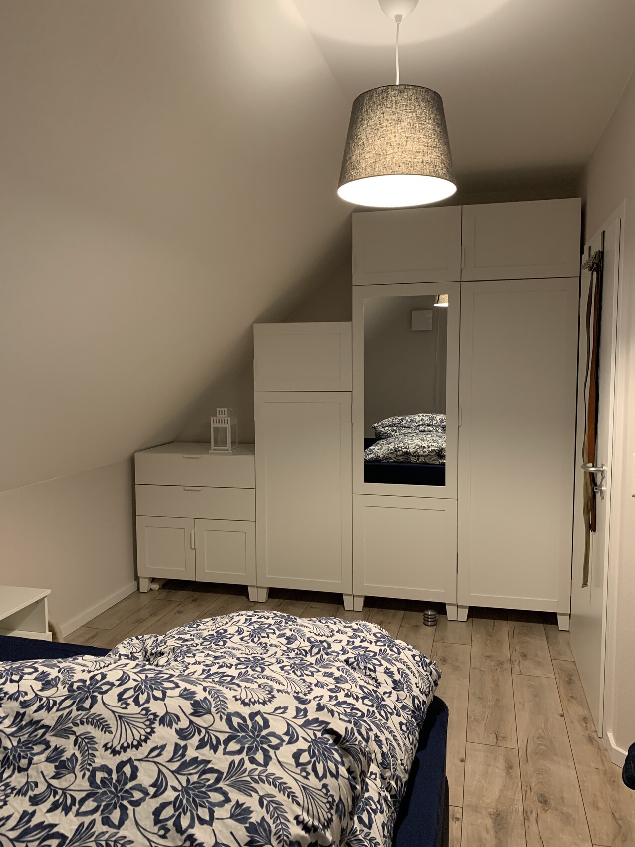 Helles Schlafzimmer mit weißem Kleiderschrank, Spiegel, Kommode; Bett mit blauem Blumendruck.