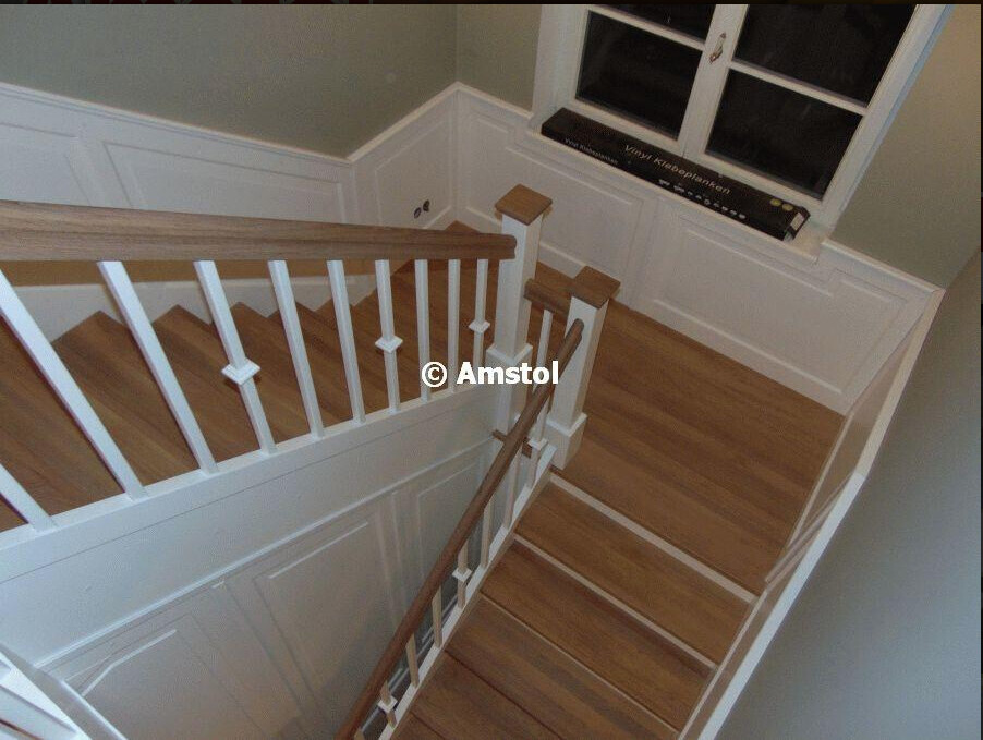 Innenansicht einer Holztreppe mit weißem Geländer und Wandvertäfelung am Treppenaufgang.