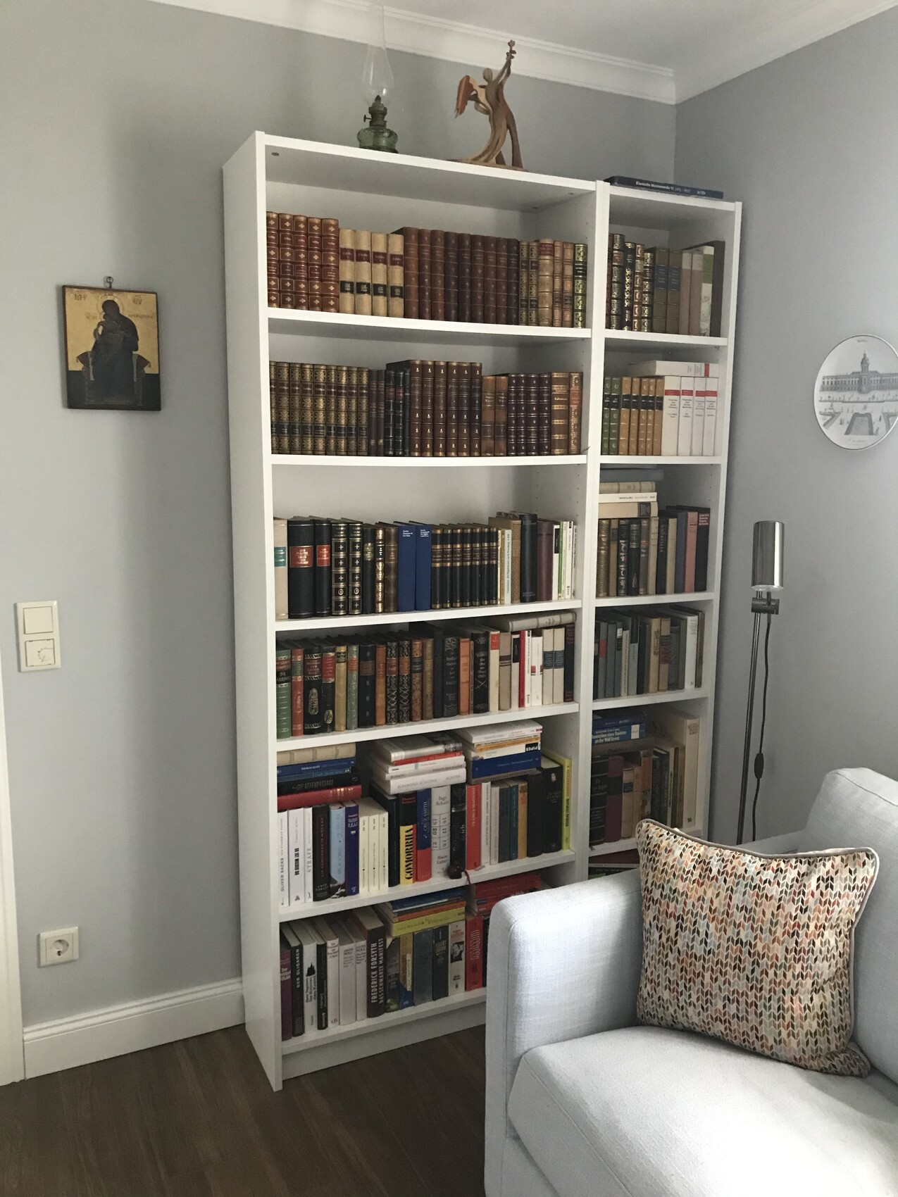 Zwei weiße Bücherregale voller Bücher, Sofa mit gemustertem Kissen, Stehlampe im Wohnzimmer