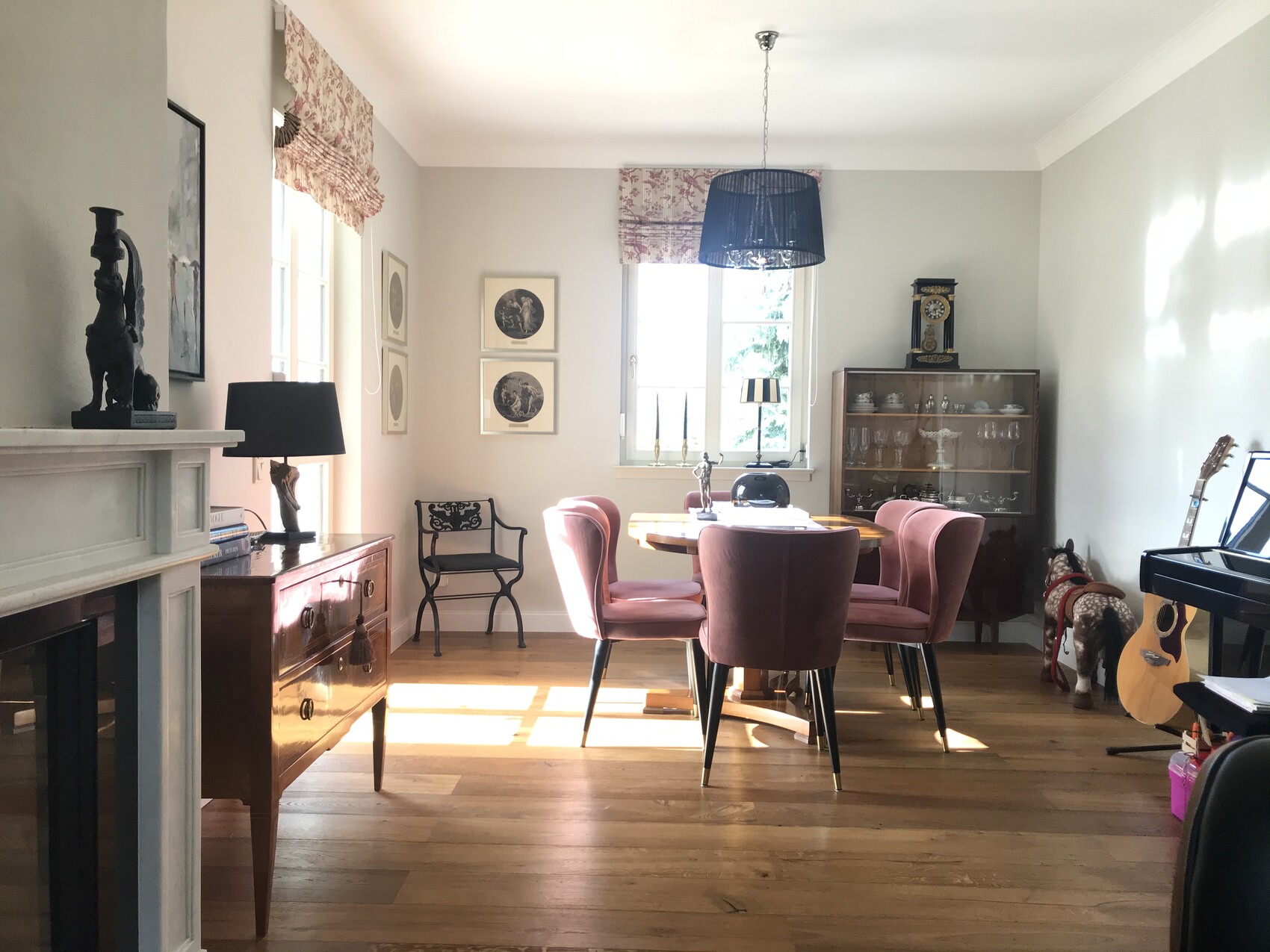 Esszimmer mit rundem Holztisch und pinken Stühlen, Glasvitrine, Klavier rechts.
