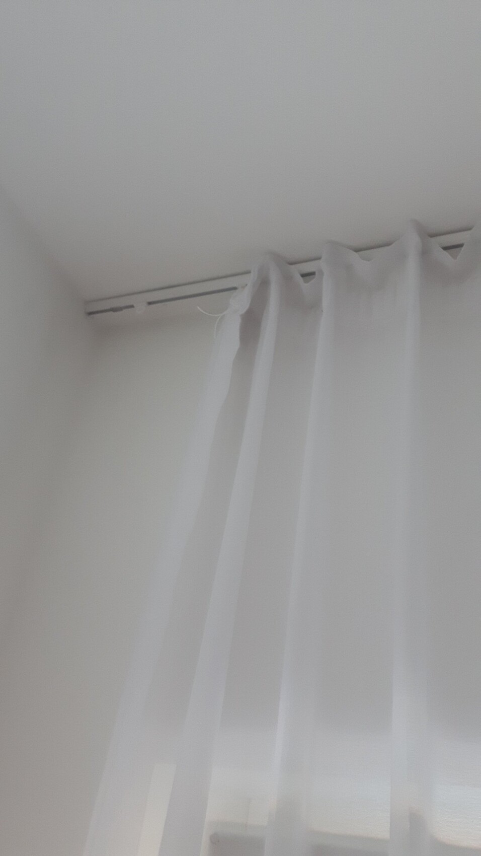 Weiße, transparente Vorhänge vor einem Fenster in einer hellen, weißen Zimmerecke.