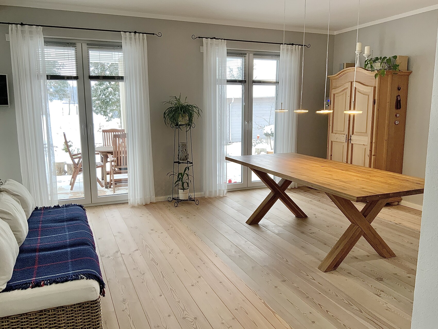 Heller Wohn- und Essbereich mit großem Holztisch, Glas-Schiebetüren, Sofa, Pflanzen und Holzschrank.