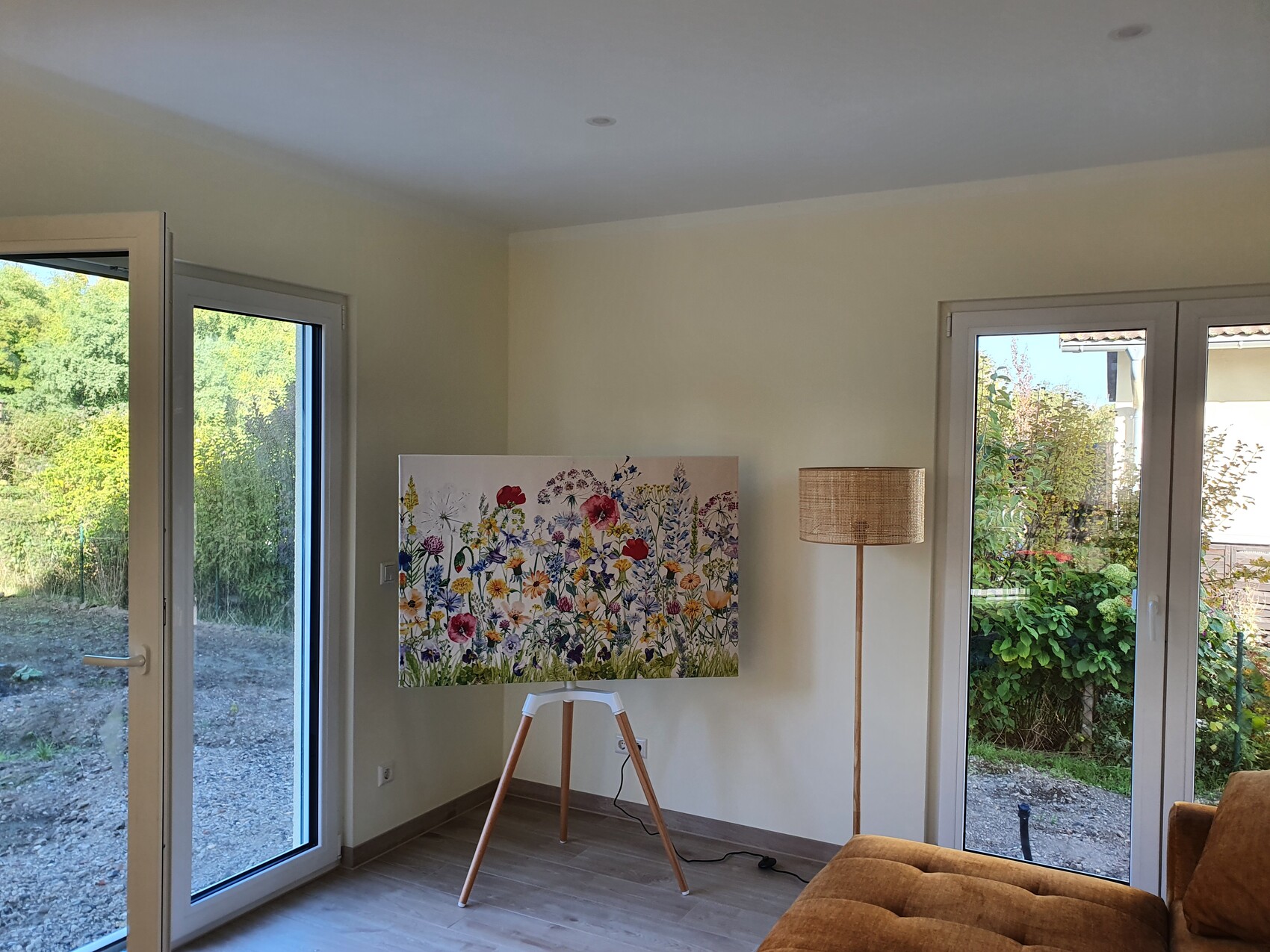 Heller Wohnraum mit Blumengemälde auf Staffelei, Stehlampe und Glas-Türen zum Garten