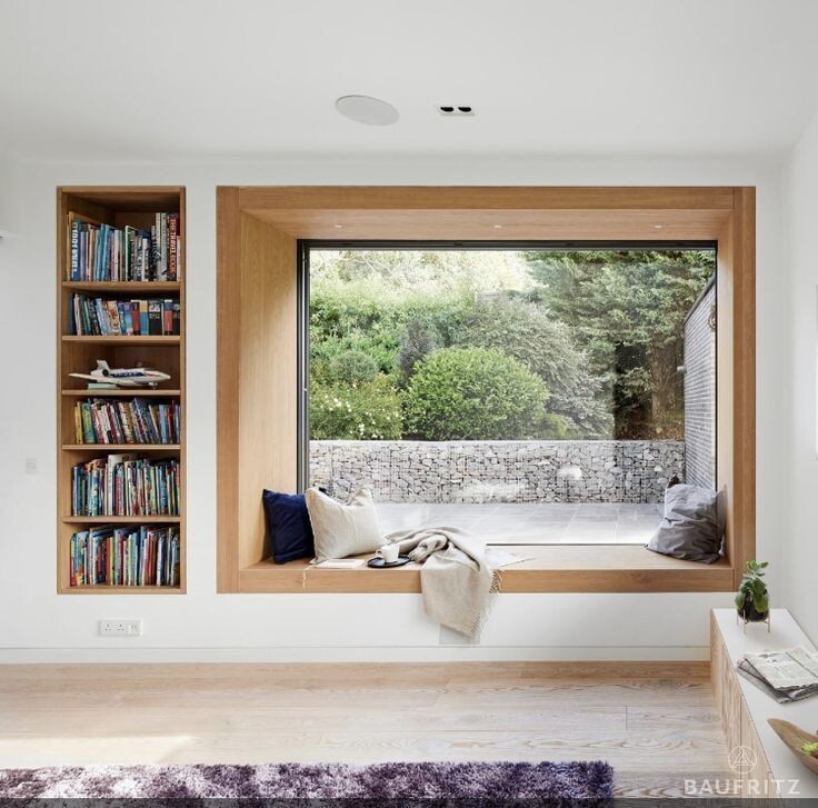 Großes Holzfenster mit Fensterbank, Gartenblick; Bücherregal links, Decke und Kissen.