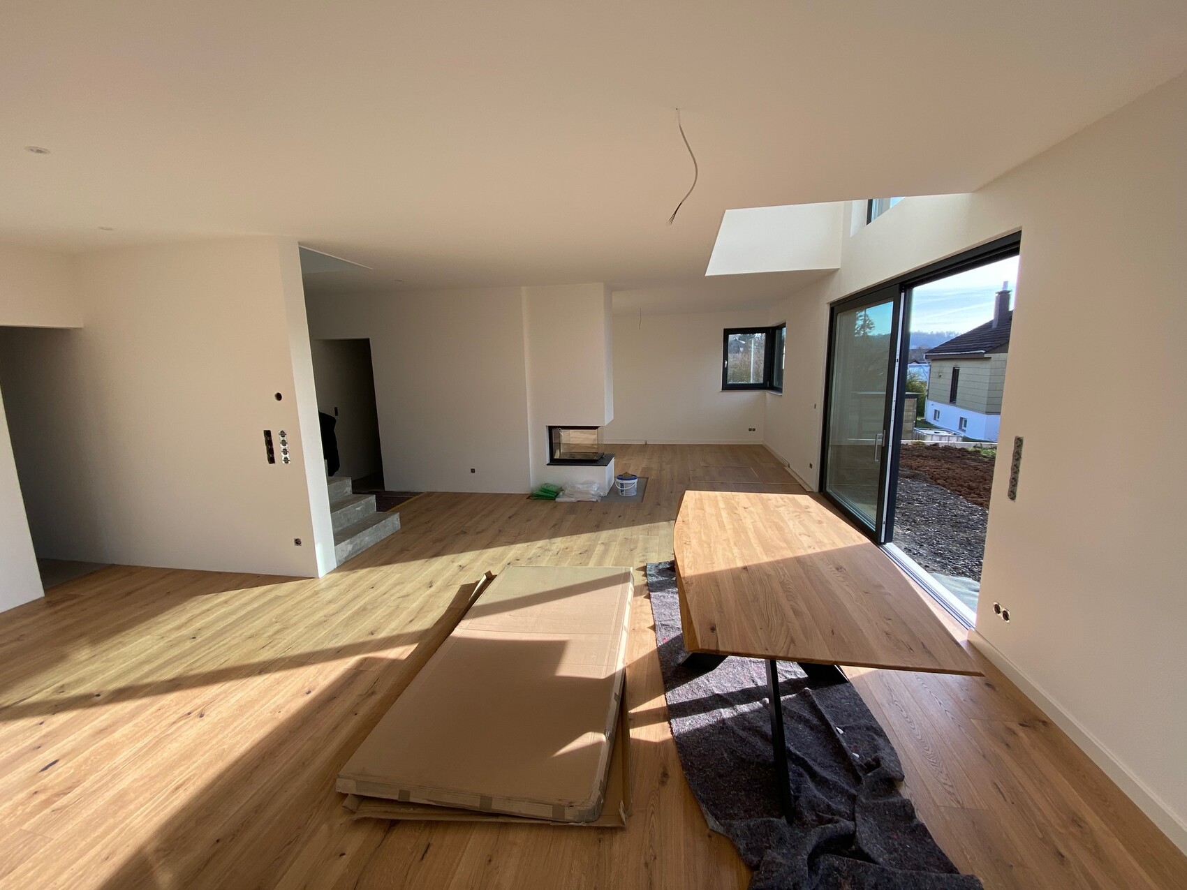 Helles unfertiges Wohnzimmer mit Holzboden und Glas-Schiebetüren nach draußen.