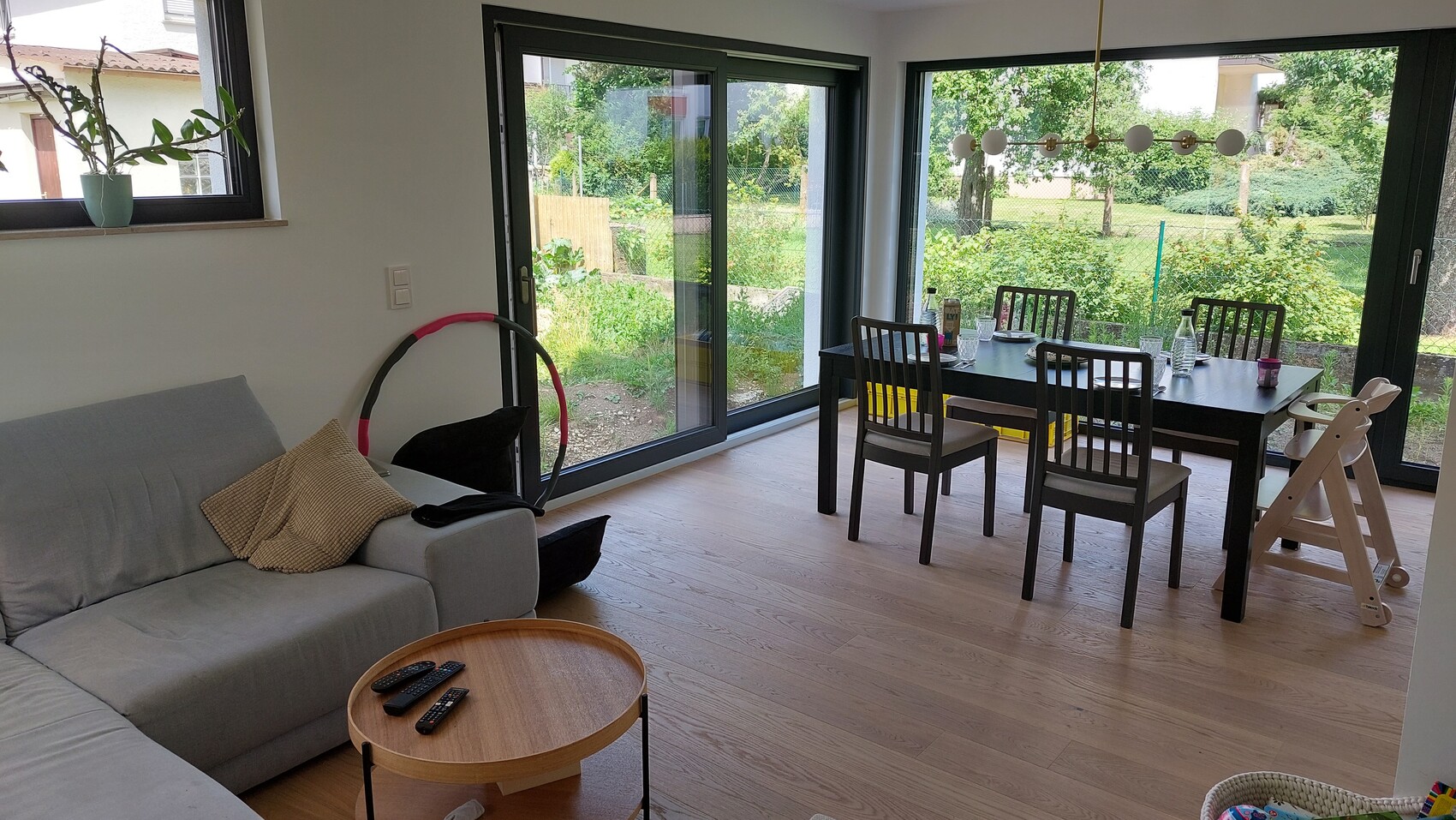 Wohnzimmer mit Esstisch und Stühle, Sofa, große Glasfront zum Garten und Hochstuhl