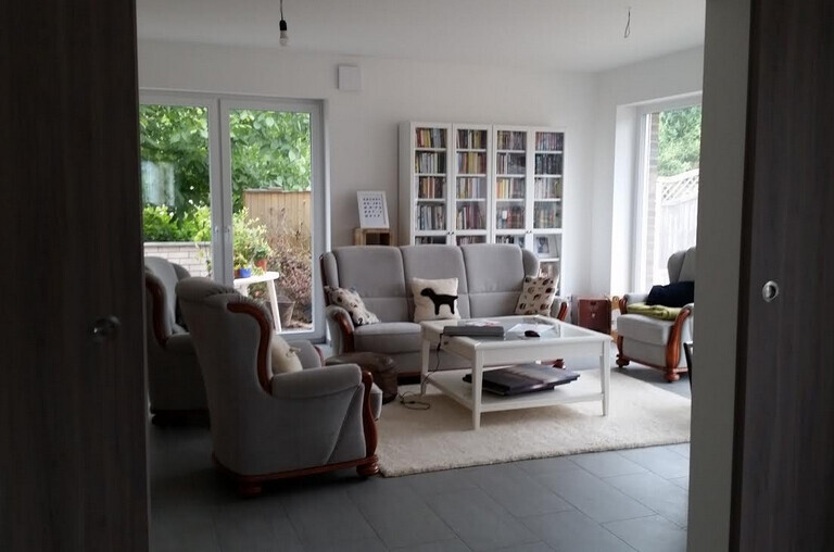 Helles Wohnzimmer mit grauen Möbeln, Couchtisch, Bücherregal und Fenster zum Garten.