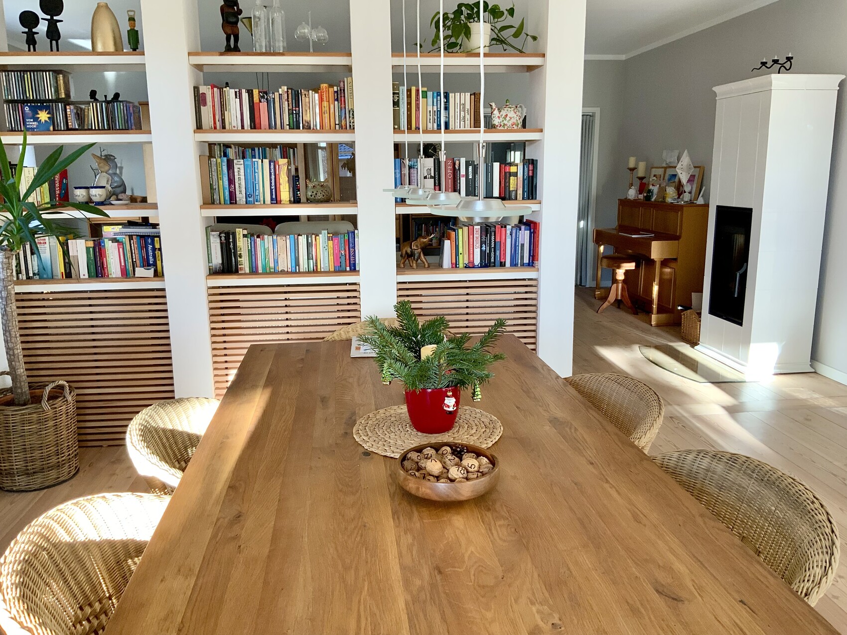 Großer Holztisch mit rotem Pflanzkübel und Nuss-Schale; Bücherregal, Korbstühle, Kamin.