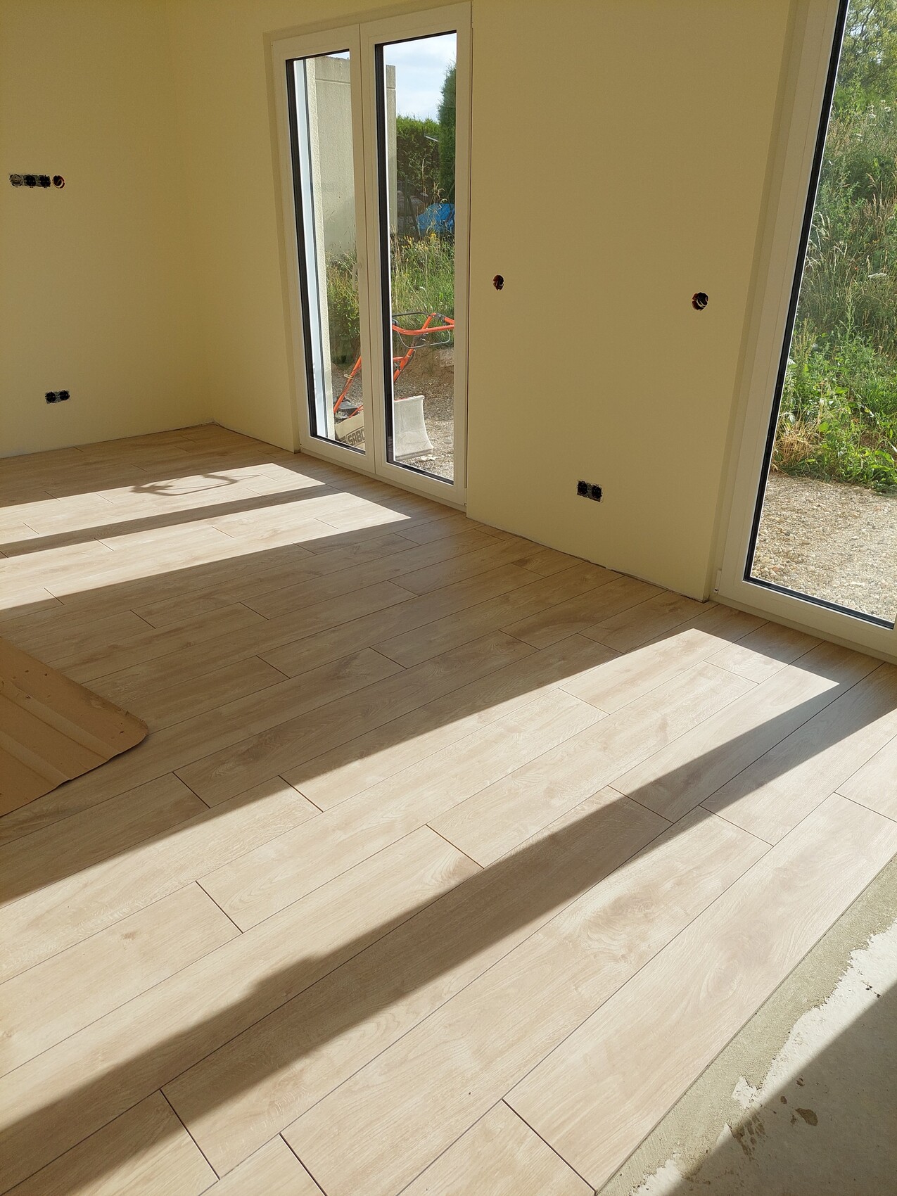 Helles Wohnzimmer mit großen Fenstern und Holzoptik-Bodenbelag.