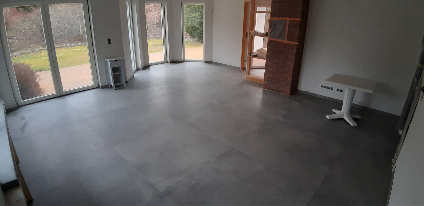 Leerer Raum mit großen Glasfenstern, grauem Boden, Backstein-Säule und weißem Tisch.