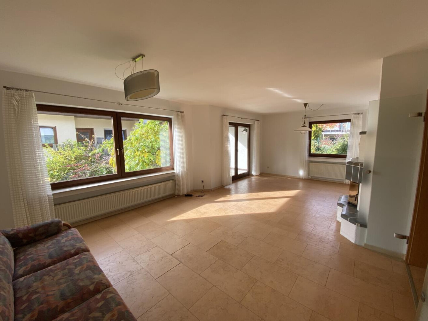 Helles Wohnzimmer mit grossen Fenstern, Terrassentuer, beige Fliesen und Sofa.