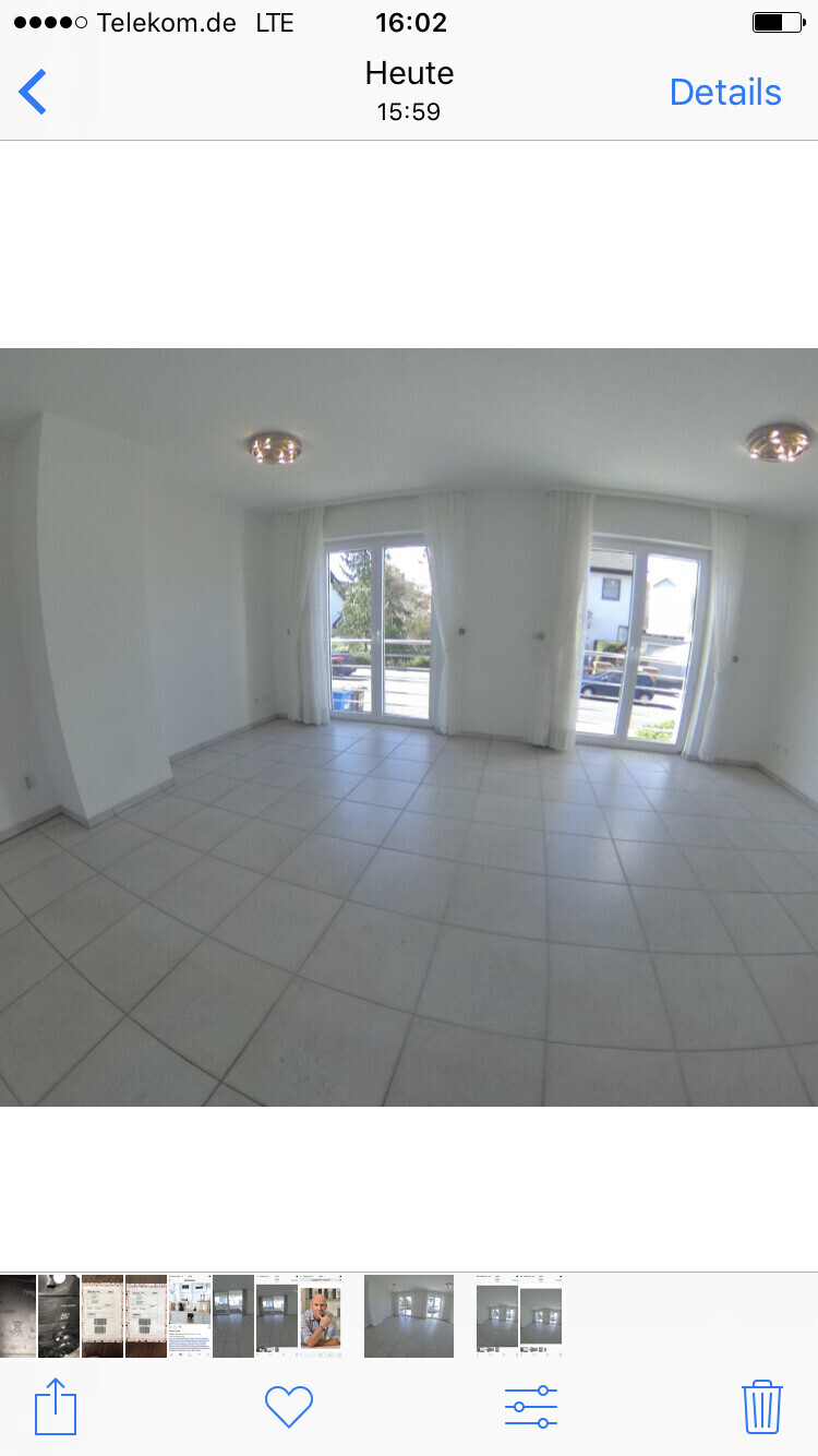 Helles Wohnzimmer mit weißen Wänden, großen Fenstern und Balkontüren.