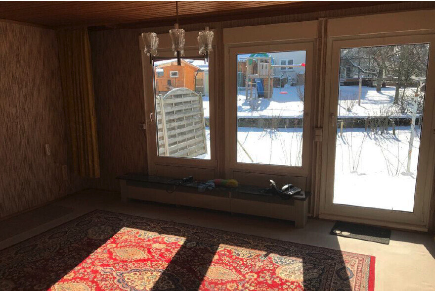 Wohnzimmer mit großen Glasfenstern und Tür, verschneiter Außenbereich, roter Teppich, Kronleuchter.