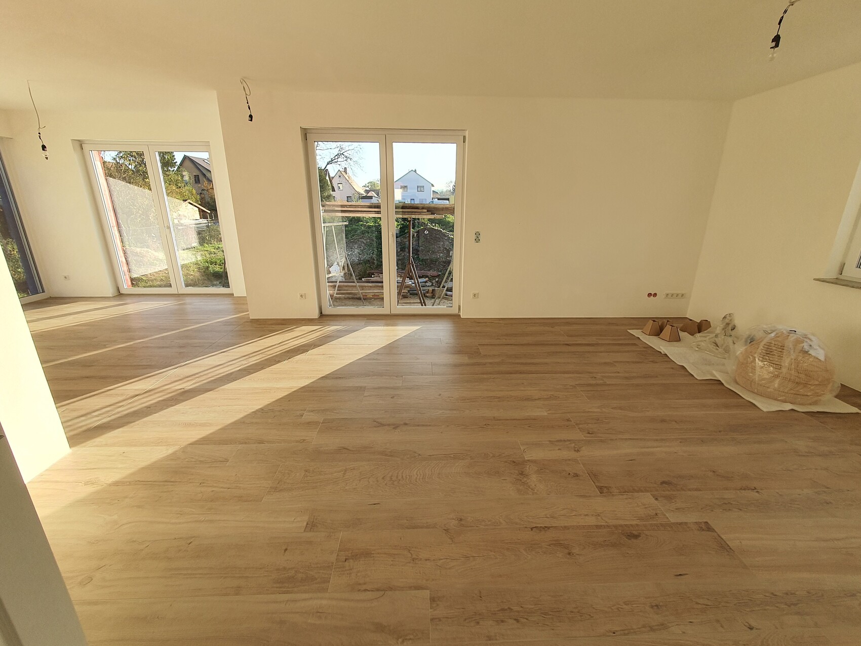 Heller leerer Raum mit Holzboden, Glas-Schiebetüren und Bau-Materialien rechts.