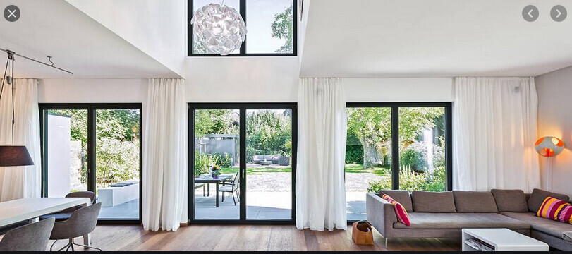Heller Wohnraum mit großen Glasfenstern und Terrassentüren, Sofa und Gartenblick.