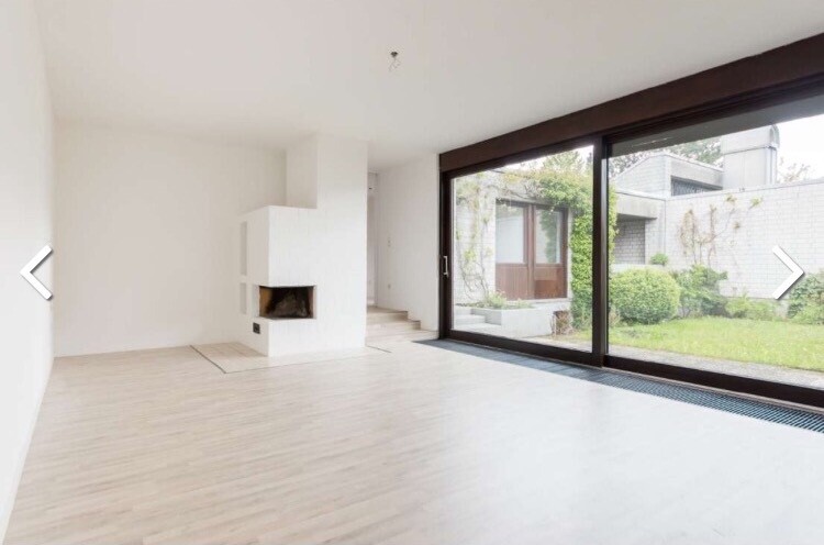 Heller Wohnraum mit Kamin, großen Glasschiebetüren zum Garten.