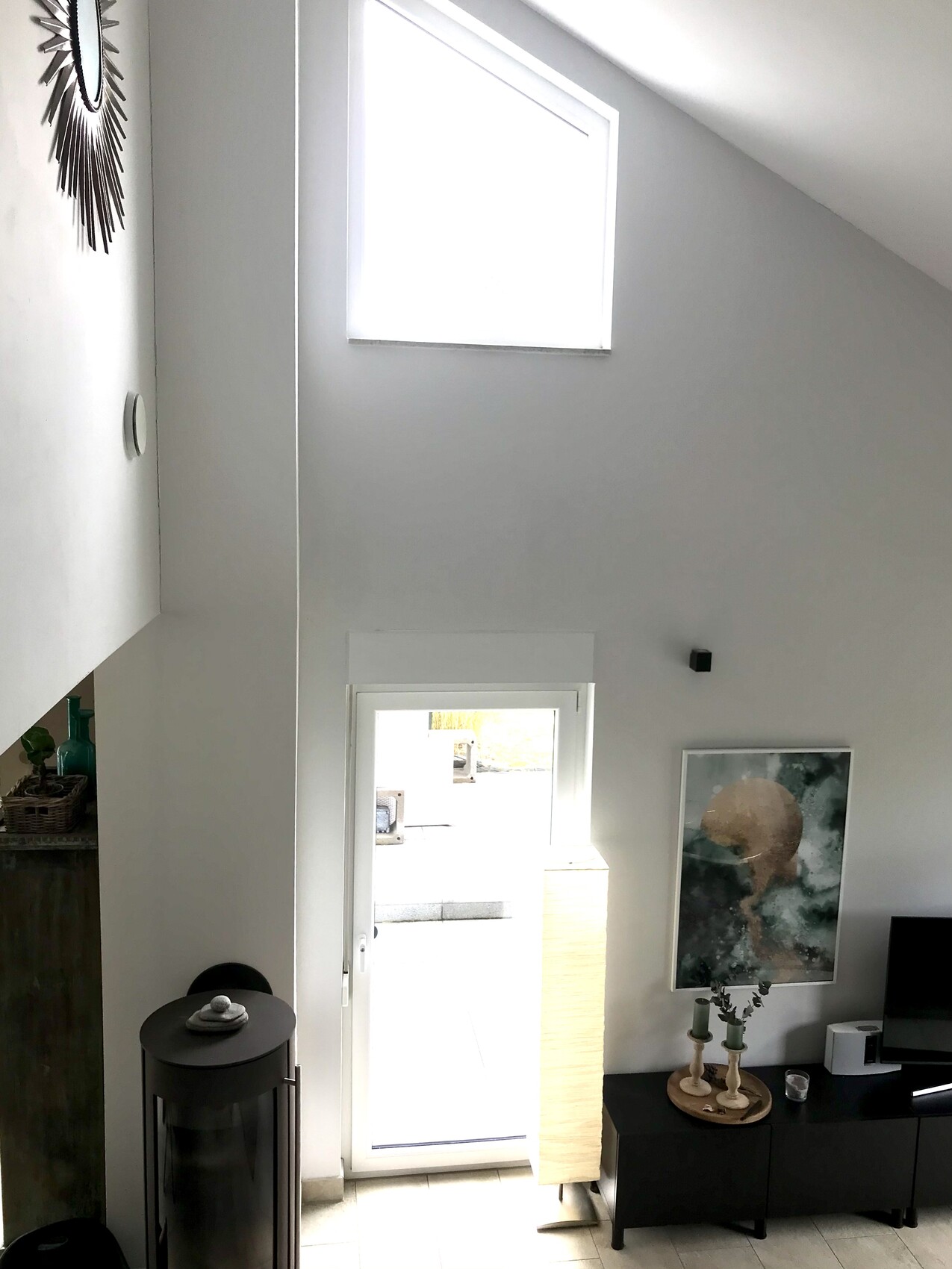 Helles Wohnzimmer mit hohen Decken, Oberlichtfenstern, Tür zur Außenwelt und Wandbild.