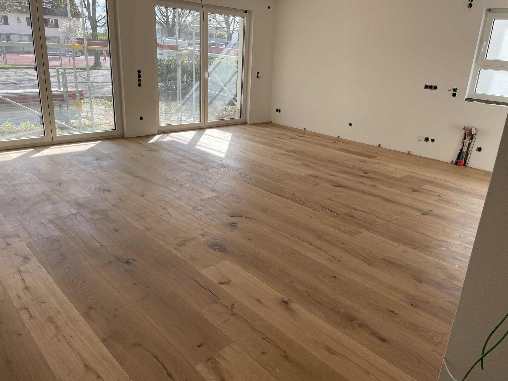 Heller Wohnraum mit Holzparkett, großen Fensterfronten und unfertiger Elektroinstallation.