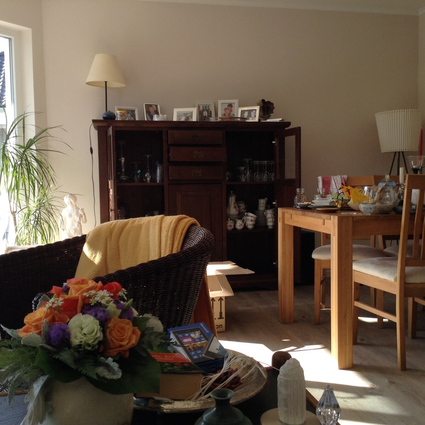 Wohnzimmer mit dunklem Sideboard, Foto-Rahmen, Gläsern, Tisch mit Geschirr und Blumenstrauß.