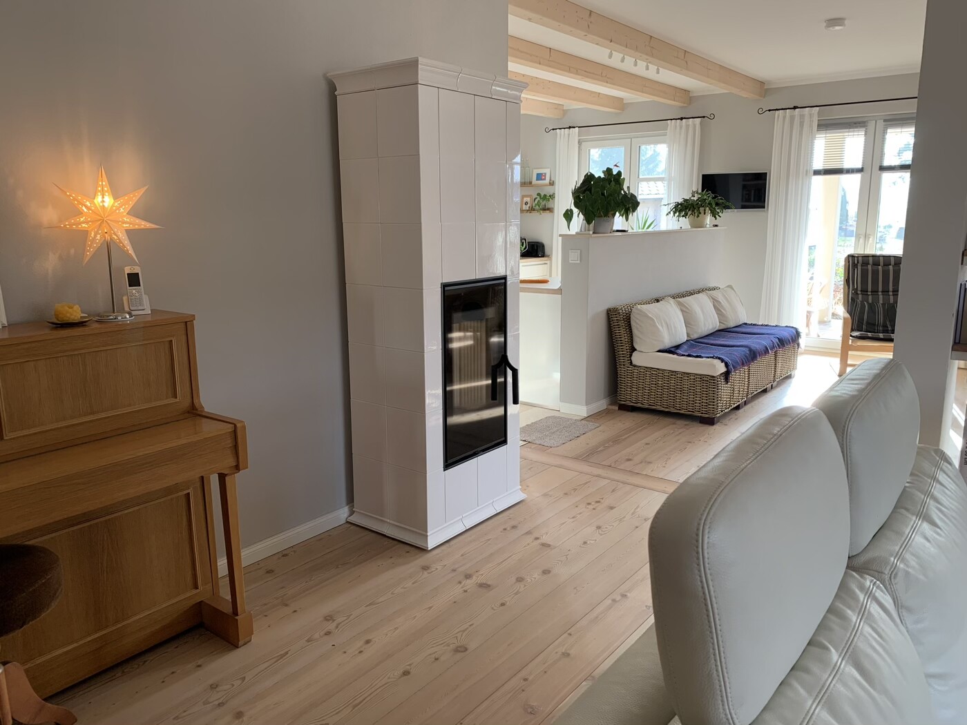 Helles Wohnzimmer mit Kaminofen, Holzboden, Korbsessel-Sofa, Stern-Lampe und Pflanzen.