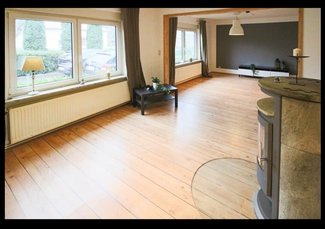 Helles Wohnzimmer mit großer Fensterfront, Holzboden, dunkler Couchtisch und Kamin.