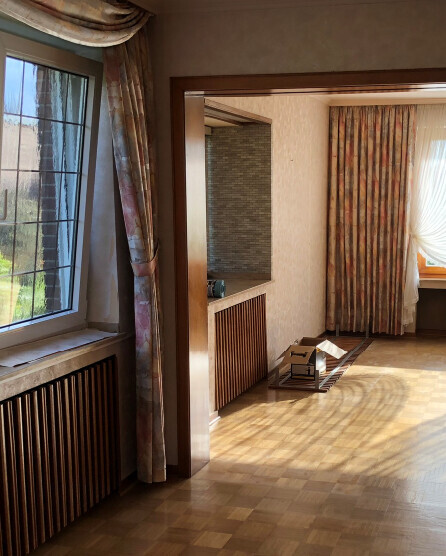 Helles Wohnzimmer mit Holzfußboden, Fenster links, Durchgang ins nächste Zimmer; Kartons.