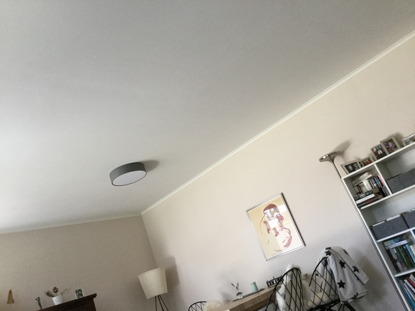 Heller Wohnraum mit Bücherregal, gerahmtem Wandbild, Stühlen mit Decke, runde Deckenleuchte.
