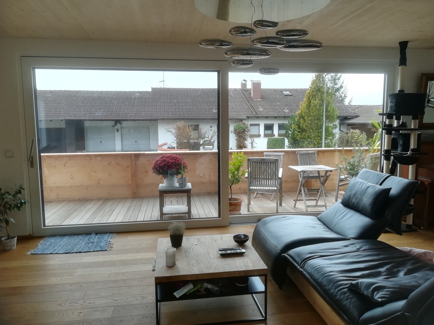 Wohnzimmer mit schwarzem Ledersofa, Glastür zum Balkon; Balkon mit Tisch, Stühlen und Pflanzen.