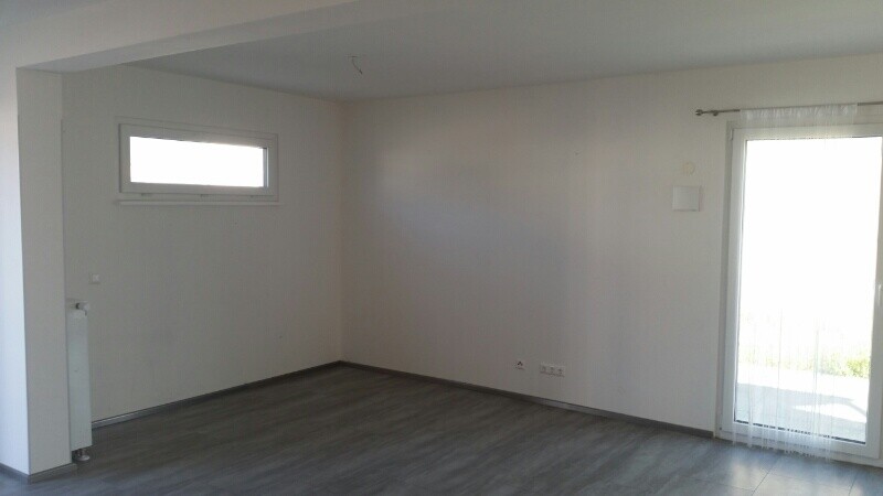 Leerer Wohnraum mit hellen Wänden, dunklem Laminat, Heizkörper links, Glas-Tür mit Vorhang rechts