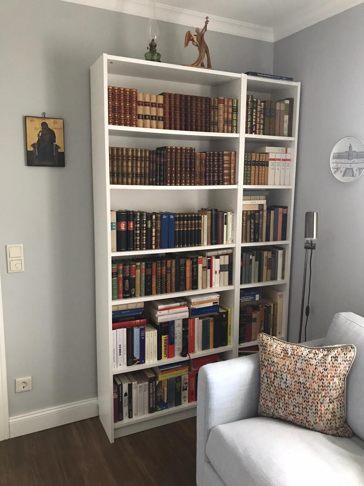 Weißes Bücherregal mit vielen Büchern im Wohnzimmer; daneben Sofa mit gemustertem Kissen.