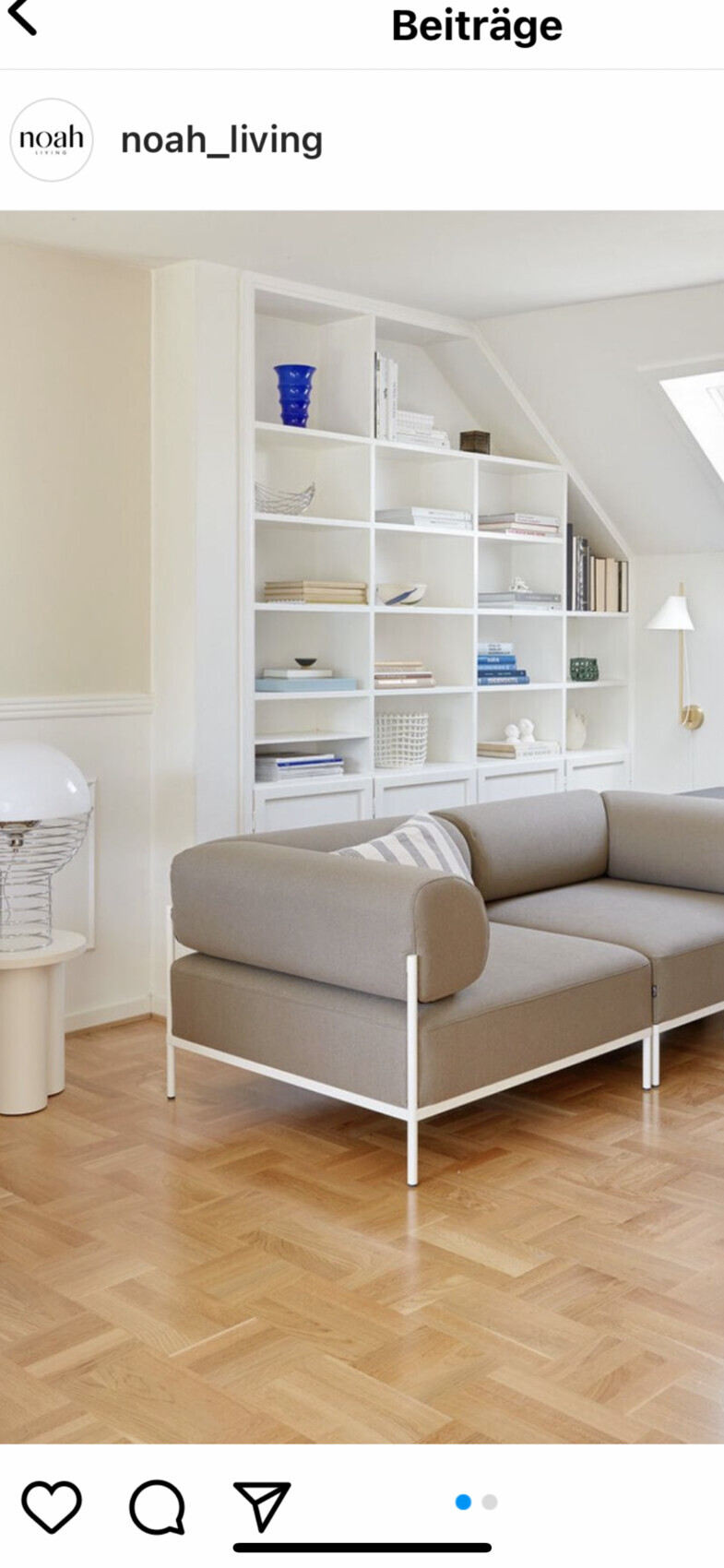 Wohnzimmer mit großem weißen Regalsystem, grauem Sofa und Holzboden; Blaue Vase.