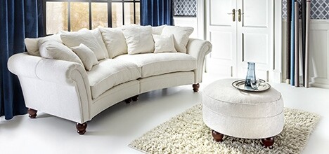 Helles Wohnzimmer mit weißem Sofa, runder Ottomane, Teppich und Vorhängen.