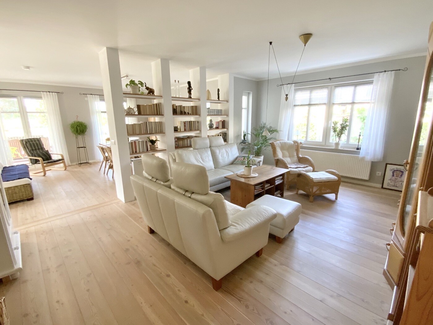 Helles Wohnzimmer mit weißem Sofa, Sessel, Couchtisch, Bücherregalen und großen Fenstern.