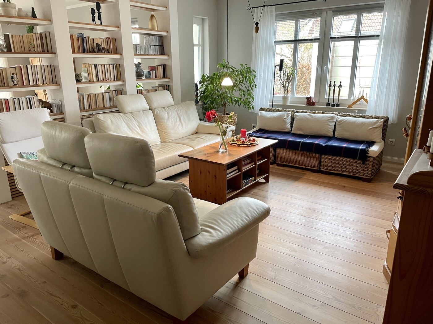Helles Wohnzimmer mit beige Ledersofas, Holzboden, Bücherregalwand, Pflanze und Fenster.