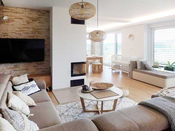 Offenes Wohnzimmer mit Kamin, Sofa, rundem Couchtisch, Hängekörbe-Lampen und Krippe am Fenster.