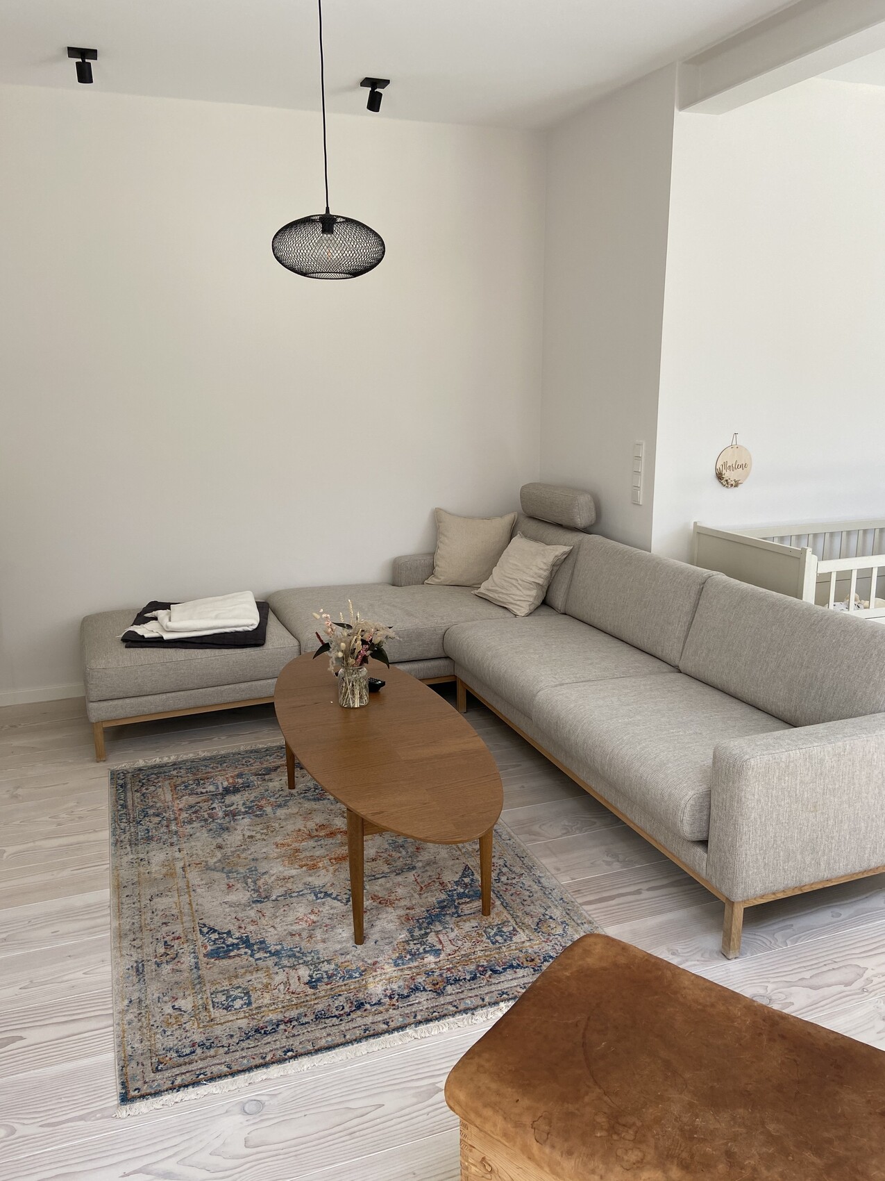 Helles modernes Wohnzimmer mit grauer Eckcouch, ovalem Holztisch und schwarzer Hängeleuchte.