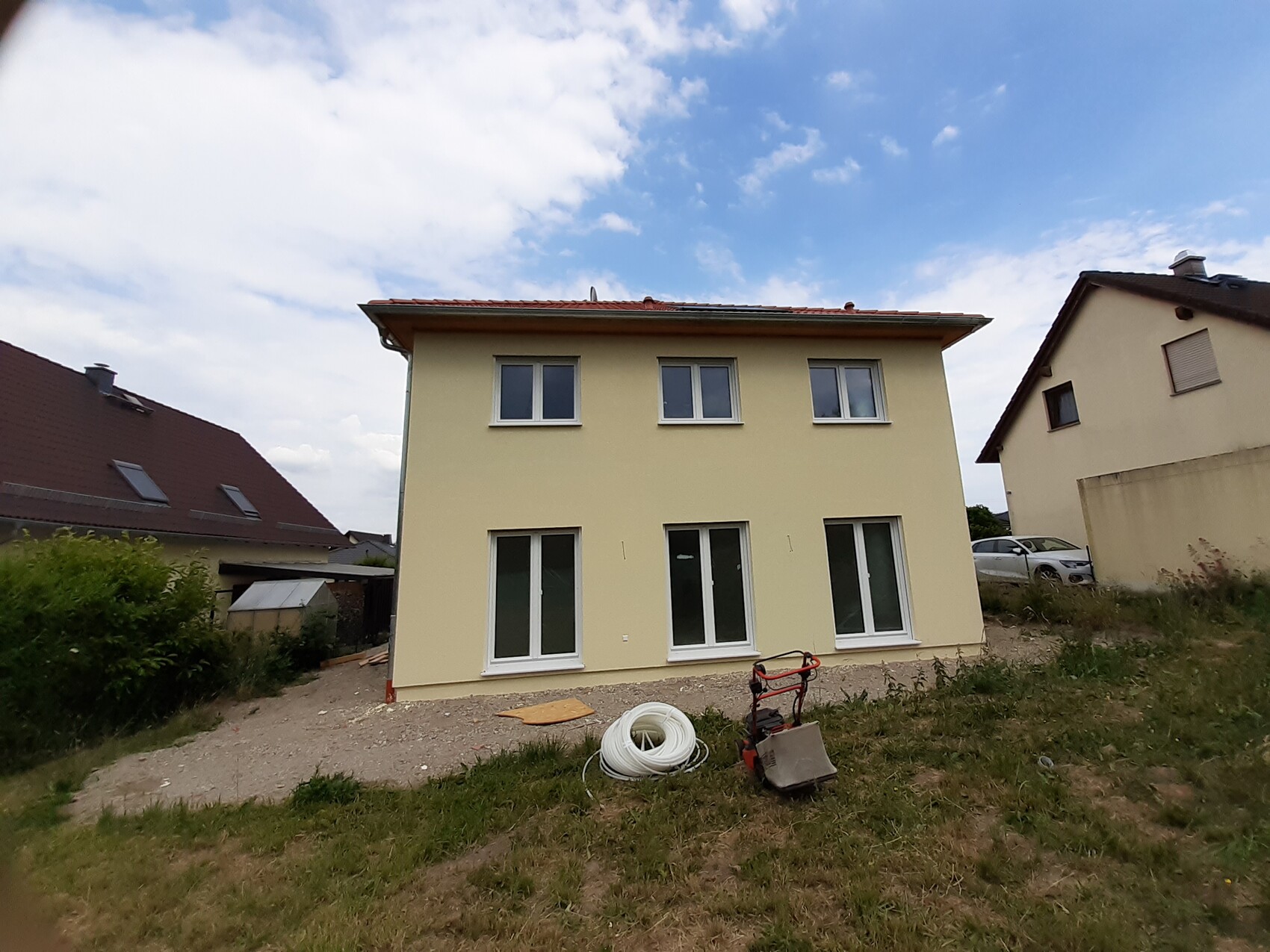 Zweistöckiges, hellgelbes Haus mit großen Fenstern; Bau- und Gartengeräte im Vordergrund.