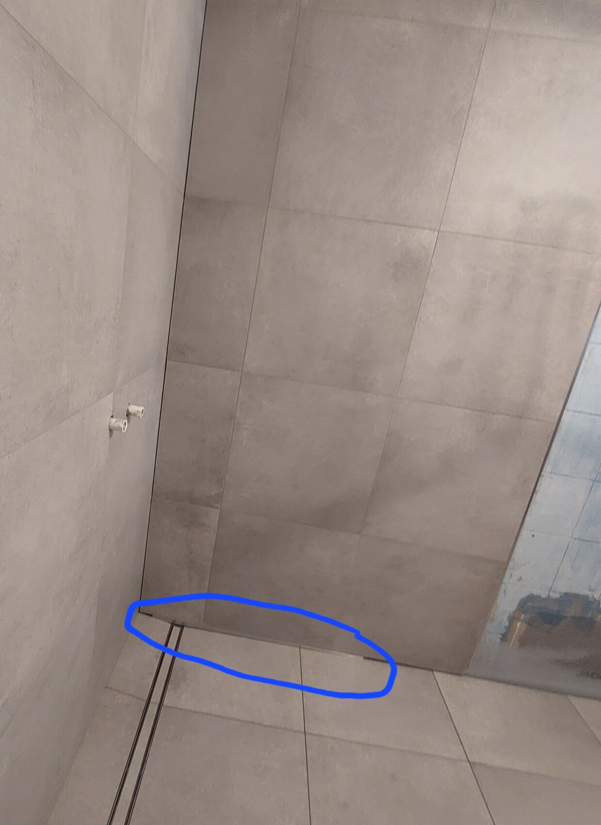 Innenraum mit grauen Fliesen an Wand und Boden; blau markierte schmale Fuge am unteren Rand.