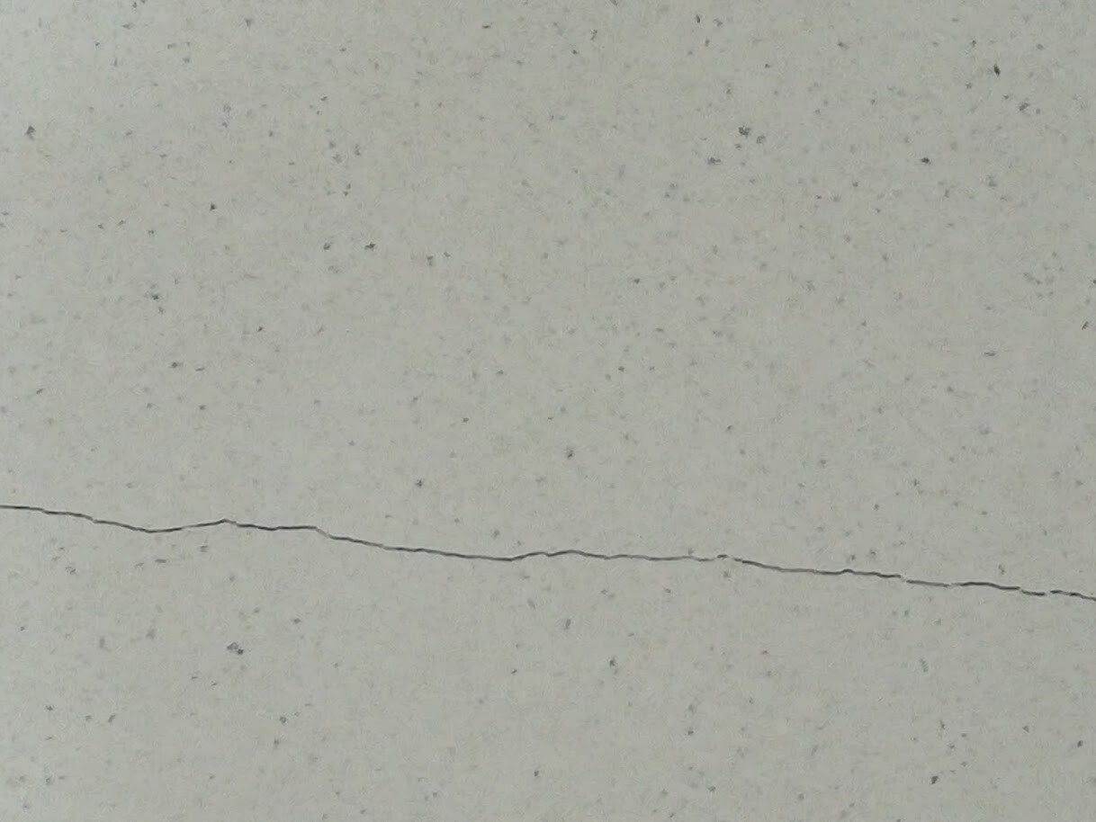Hellgraue Betonwand mit feiner Sprenkelstruktur und einer horizontalen Risslinie.