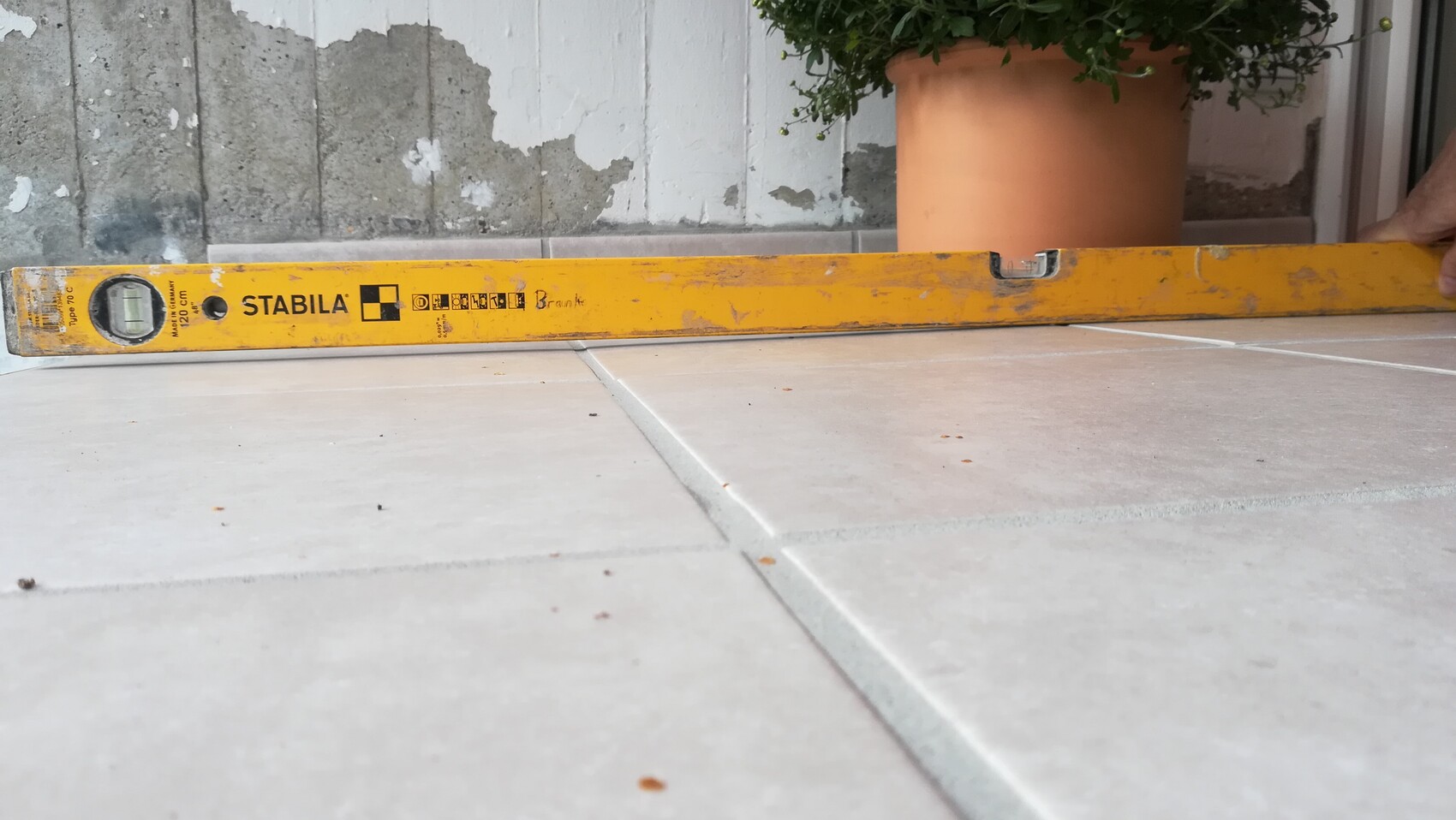 Eine gelbe STABILA-Wasserwaage liegt flach auf Fliesen; im Hintergrund Pflanzentopf.