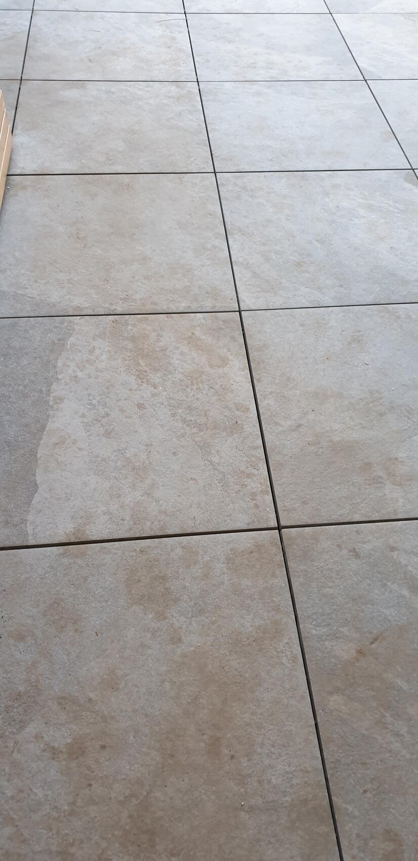 Großer Boden aus hellbeigen Fliesen mit dunklen Fugen; seitlich Schatten sichtbar.