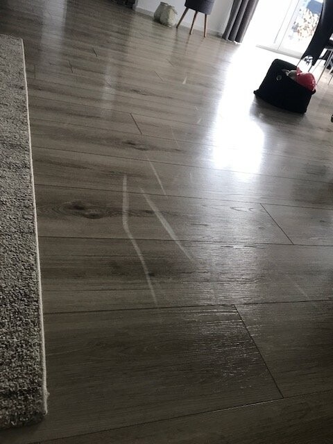 Heller Laminatboden im Wohnzimmer neben Teppichkante und Fenster.