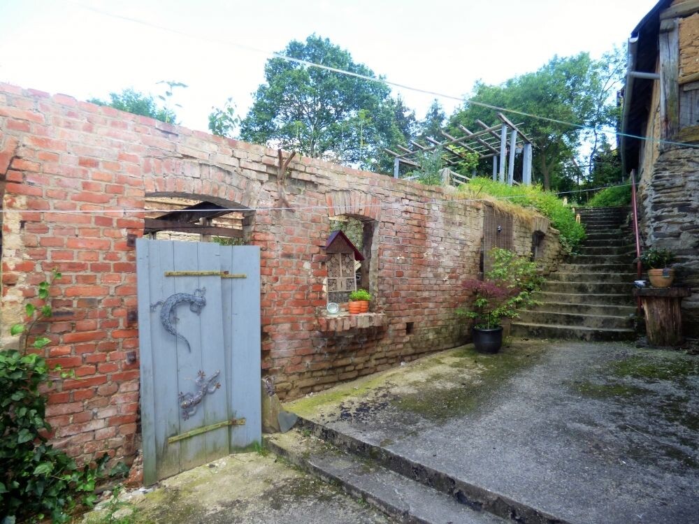 Gartenhof mit roter Backsteinmauer, blaugrauer Holztür, Treppenstufen und Topfpflanzen.