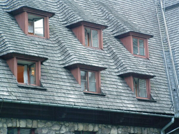 Dach eines Gebäudes mit grauem Schiefer, roten Gaubenfenstern und Steinunterbau.
